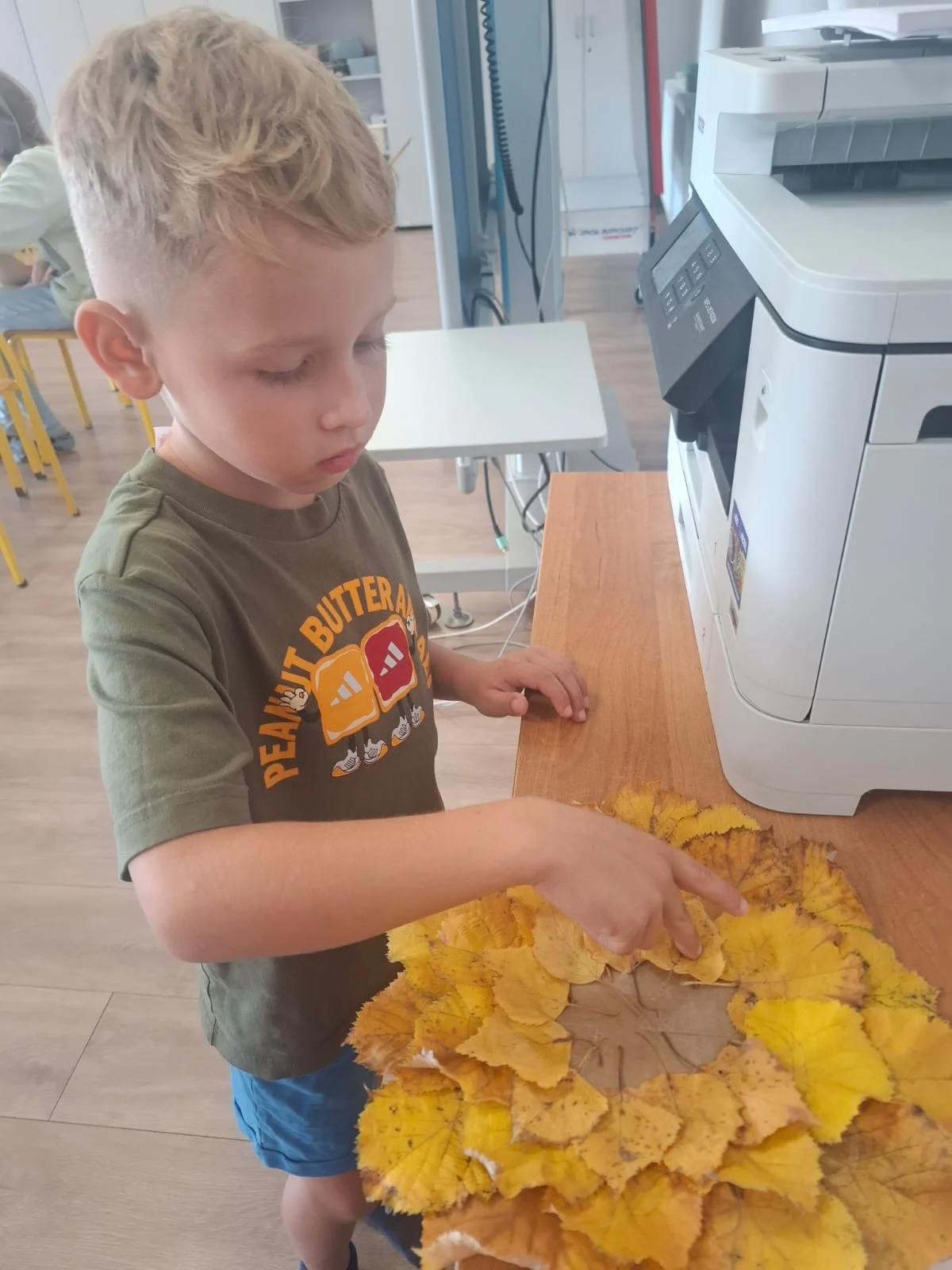 Dzieci ze świetlicy „LIPA” zbierają jesienne liście i szyszki, a następnie wspólnie tworzą z nich słonecznik. Zdjęcia przedstawiają zbieranie materiałów, układanie liści i szyszek oraz gotową pracę z łodygą z patyka i dekoracją z mniejszych kwiatów.