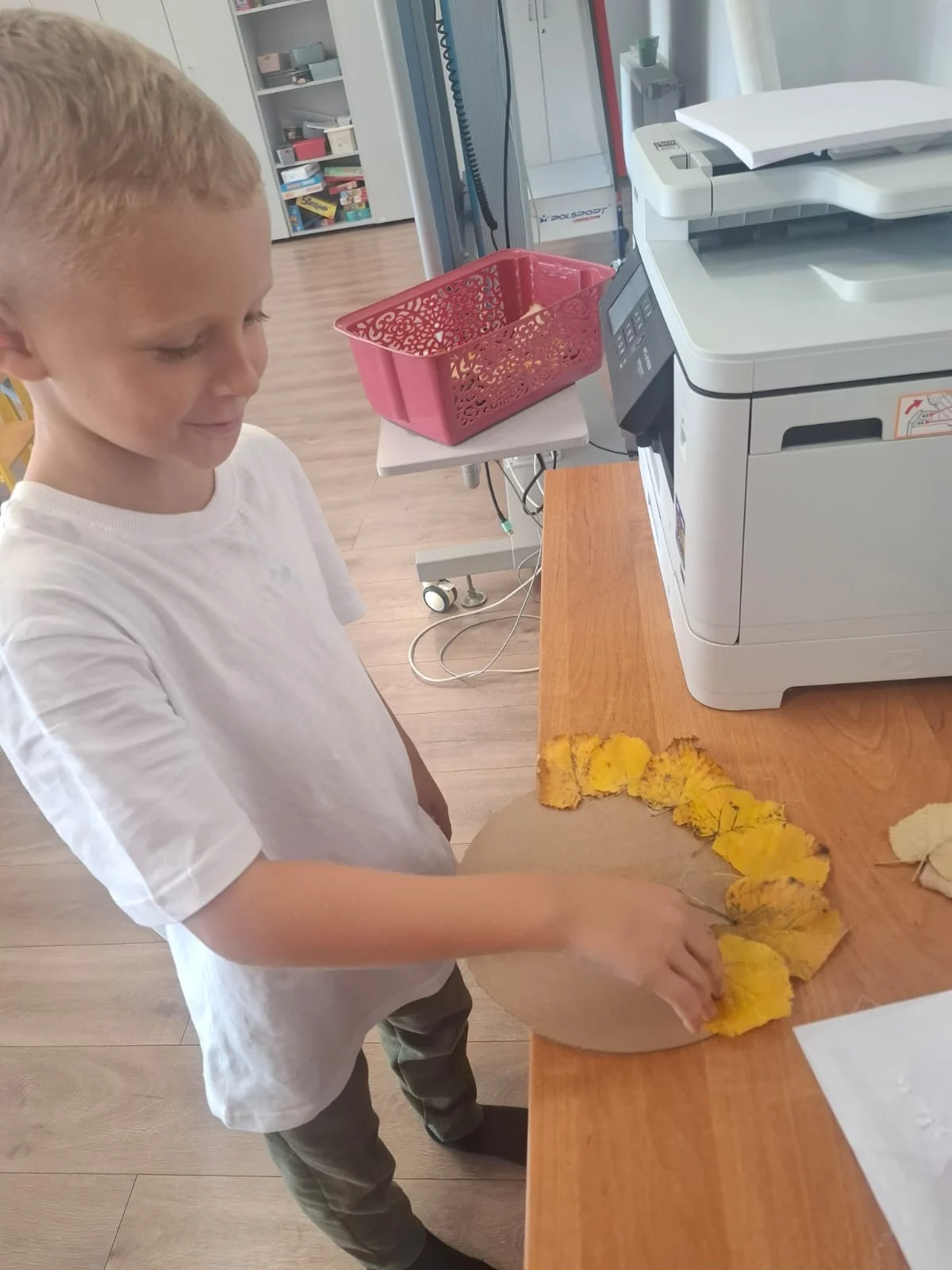 Dzieci ze świetlicy „LIPA” zbierają jesienne liście i szyszki, a następnie wspólnie tworzą z nich słonecznik. Zdjęcia przedstawiają zbieranie materiałów, układanie liści i szyszek oraz gotową pracę z łodygą z patyka i dekoracją z mniejszych kwiatów.