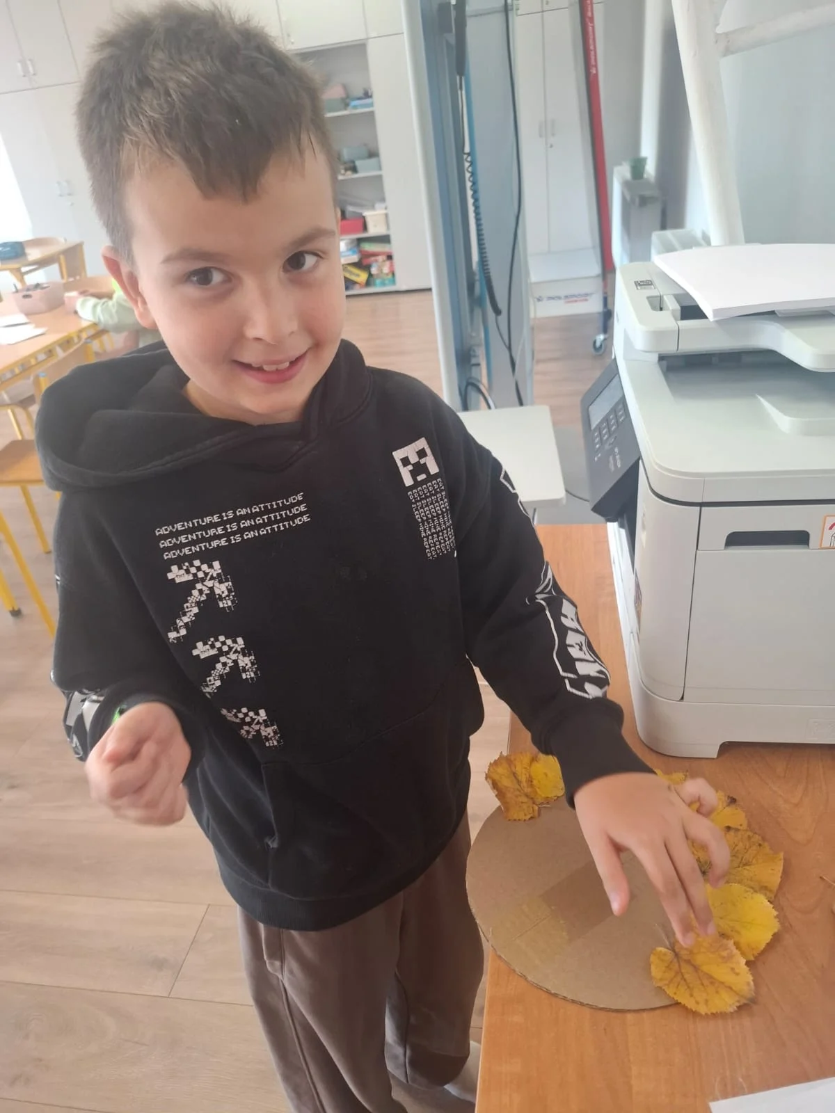 Dzieci ze świetlicy „LIPA” zbierają jesienne liście i szyszki, a następnie wspólnie tworzą z nich słonecznik. Zdjęcia przedstawiają zbieranie materiałów, układanie liści i szyszek oraz gotową pracę z łodygą z patyka i dekoracją z mniejszych kwiatów.