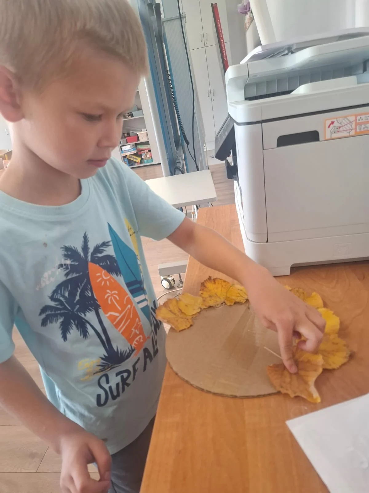 Dzieci ze świetlicy „LIPA” zbierają jesienne liście i szyszki, a następnie wspólnie tworzą z nich słonecznik. Zdjęcia przedstawiają zbieranie materiałów, układanie liści i szyszek oraz gotową pracę z łodygą z patyka i dekoracją z mniejszych kwiatów.