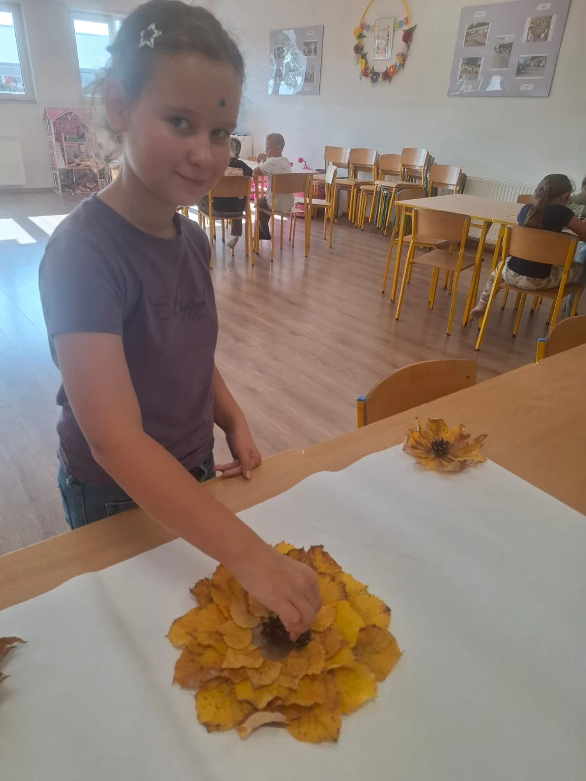 Dzieci ze świetlicy „LIPA” zbierają jesienne liście i szyszki, a następnie wspólnie tworzą z nich słonecznik. Zdjęcia przedstawiają zbieranie materiałów, układanie liści i szyszek oraz gotową pracę z łodygą z patyka i dekoracją z mniejszych kwiatów.