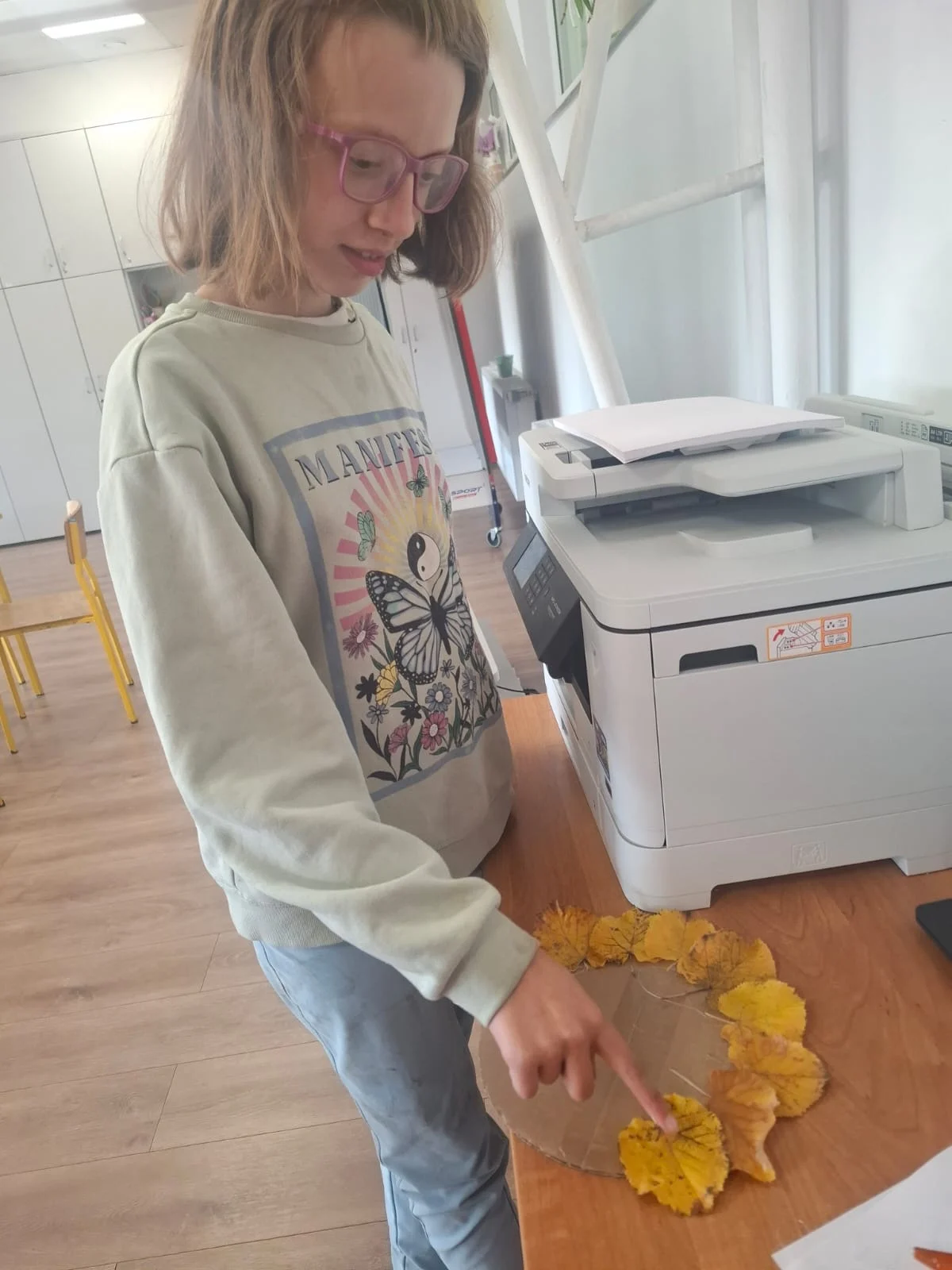 Dzieci ze świetlicy „LIPA” zbierają jesienne liście i szyszki, a następnie wspólnie tworzą z nich słonecznik. Zdjęcia przedstawiają zbieranie materiałów, układanie liści i szyszek oraz gotową pracę z łodygą z patyka i dekoracją z mniejszych kwiatów.
