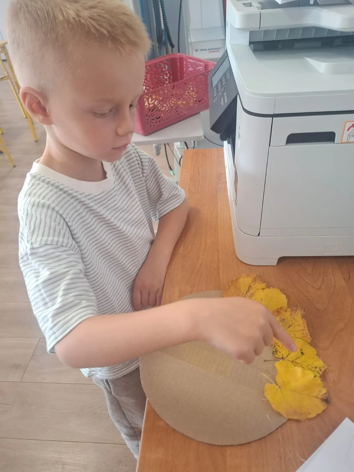 Dzieci ze świetlicy „LIPA” zbierają jesienne liście i szyszki, a następnie wspólnie tworzą z nich słonecznik. Zdjęcia przedstawiają zbieranie materiałów, układanie liści i szyszek oraz gotową pracę z łodygą z patyka i dekoracją z mniejszych kwiatów.
