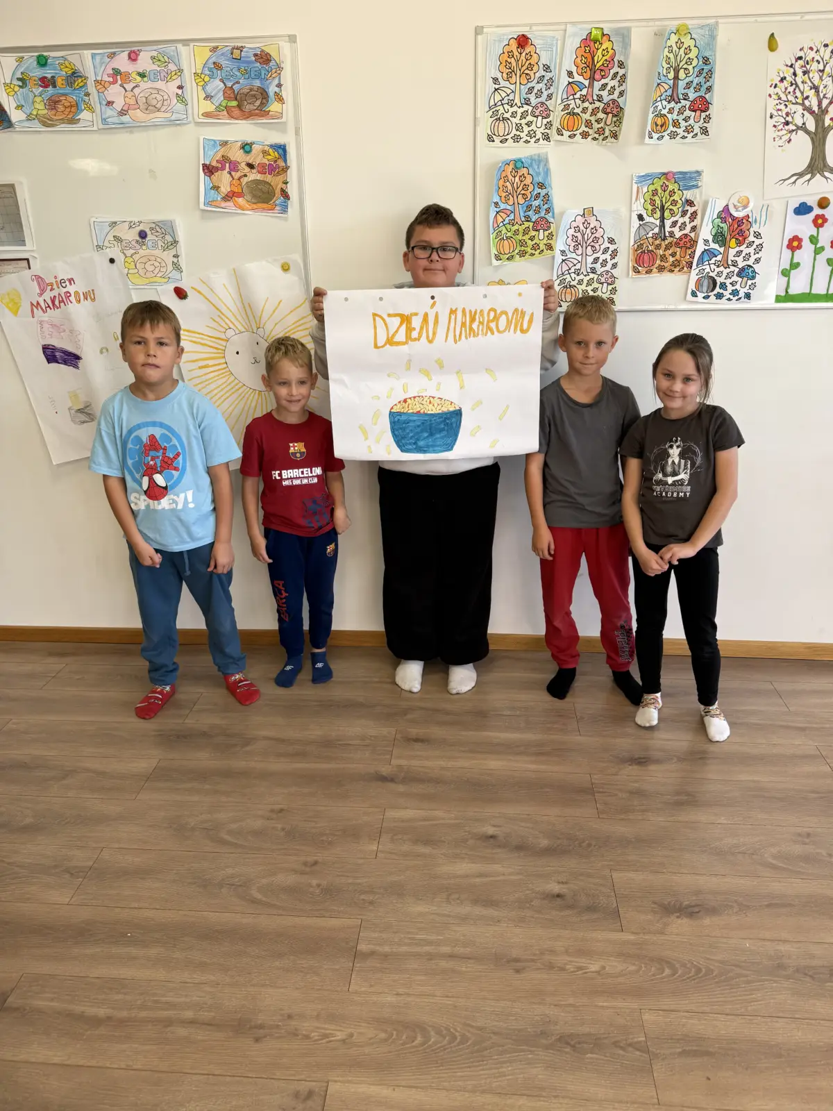 Zdjęcia z Dnia Makaronu w świetlicy. Dzieci pracują w grupach nad kolorowymi plakatami przedstawiającymi makarony i przygotowane z nich dania oraz prezentują gotowe prace.