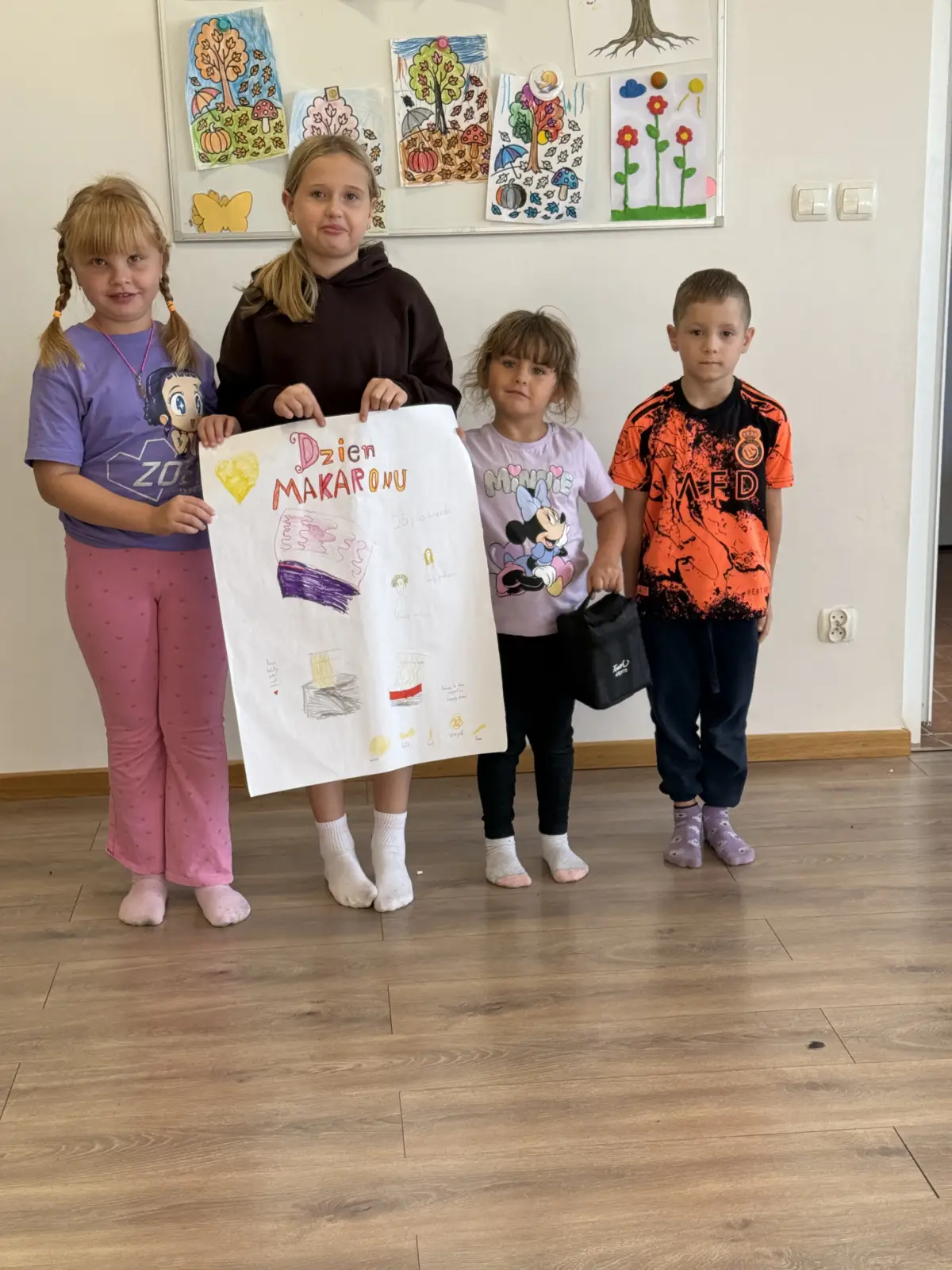Zdjęcia z Dnia Makaronu w świetlicy. Dzieci pracują w grupach nad kolorowymi plakatami przedstawiającymi makarony i przygotowane z nich dania oraz prezentują gotowe prace.
