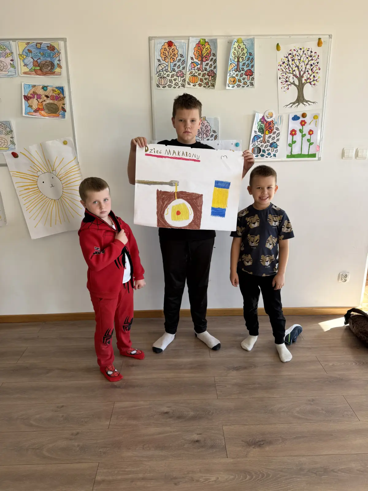 Zdjęcia z Dnia Makaronu w świetlicy. Dzieci pracują w grupach nad kolorowymi plakatami przedstawiającymi makarony i przygotowane z nich dania oraz prezentują gotowe prace.