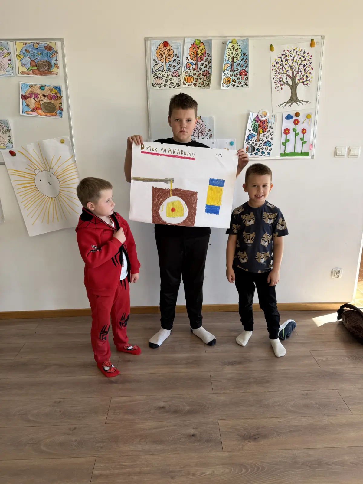 Zdjęcia z Dnia Makaronu w świetlicy. Dzieci pracują w grupach nad kolorowymi plakatami przedstawiającymi makarony i przygotowane z nich dania oraz prezentują gotowe prace.